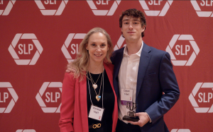 A man and a woman smiling in front of a red backdrop.